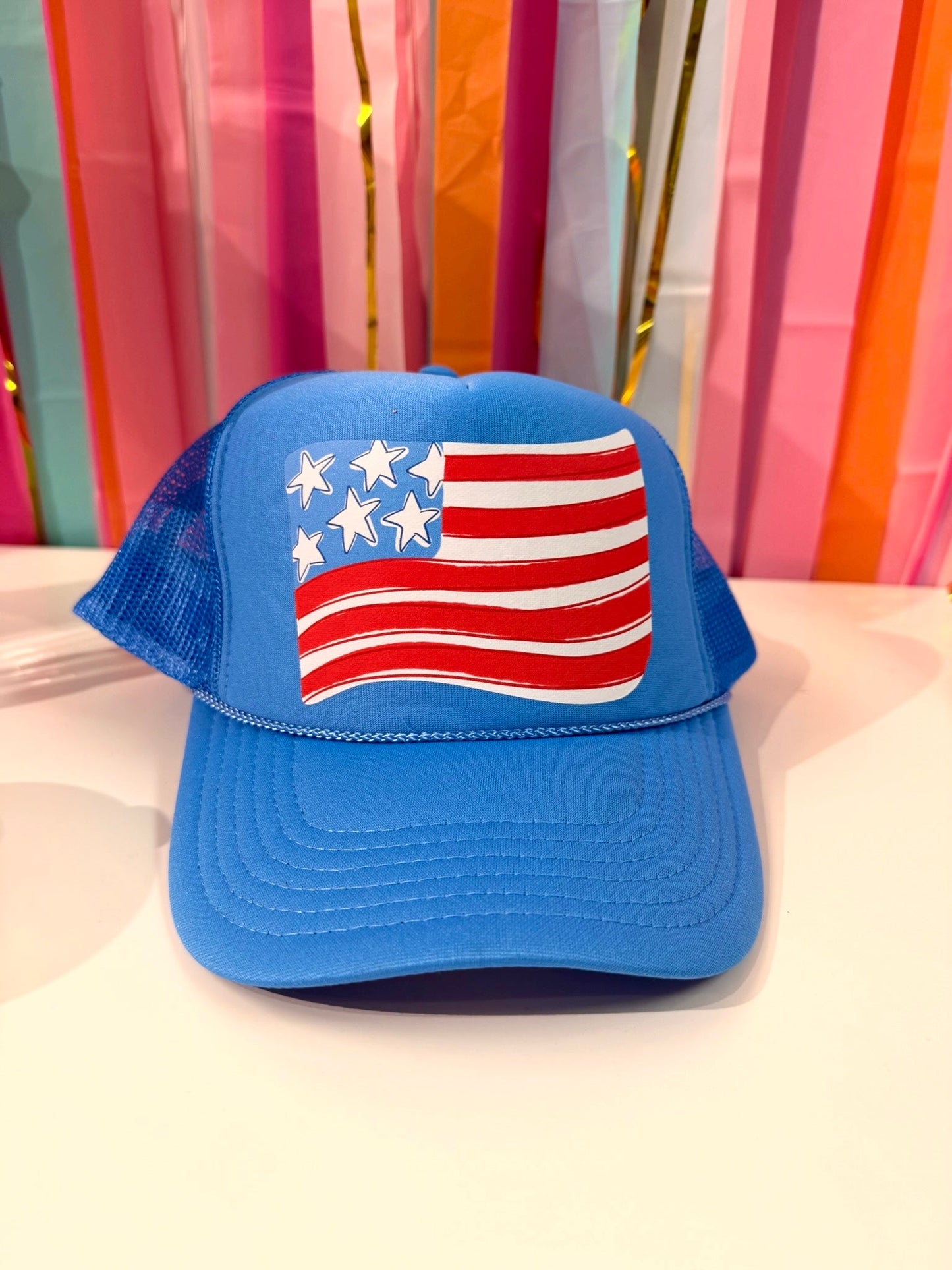 Blue American flag trucker hat with a whimsical waving flag design, perfect for patriotic celebrations or summer accessories.