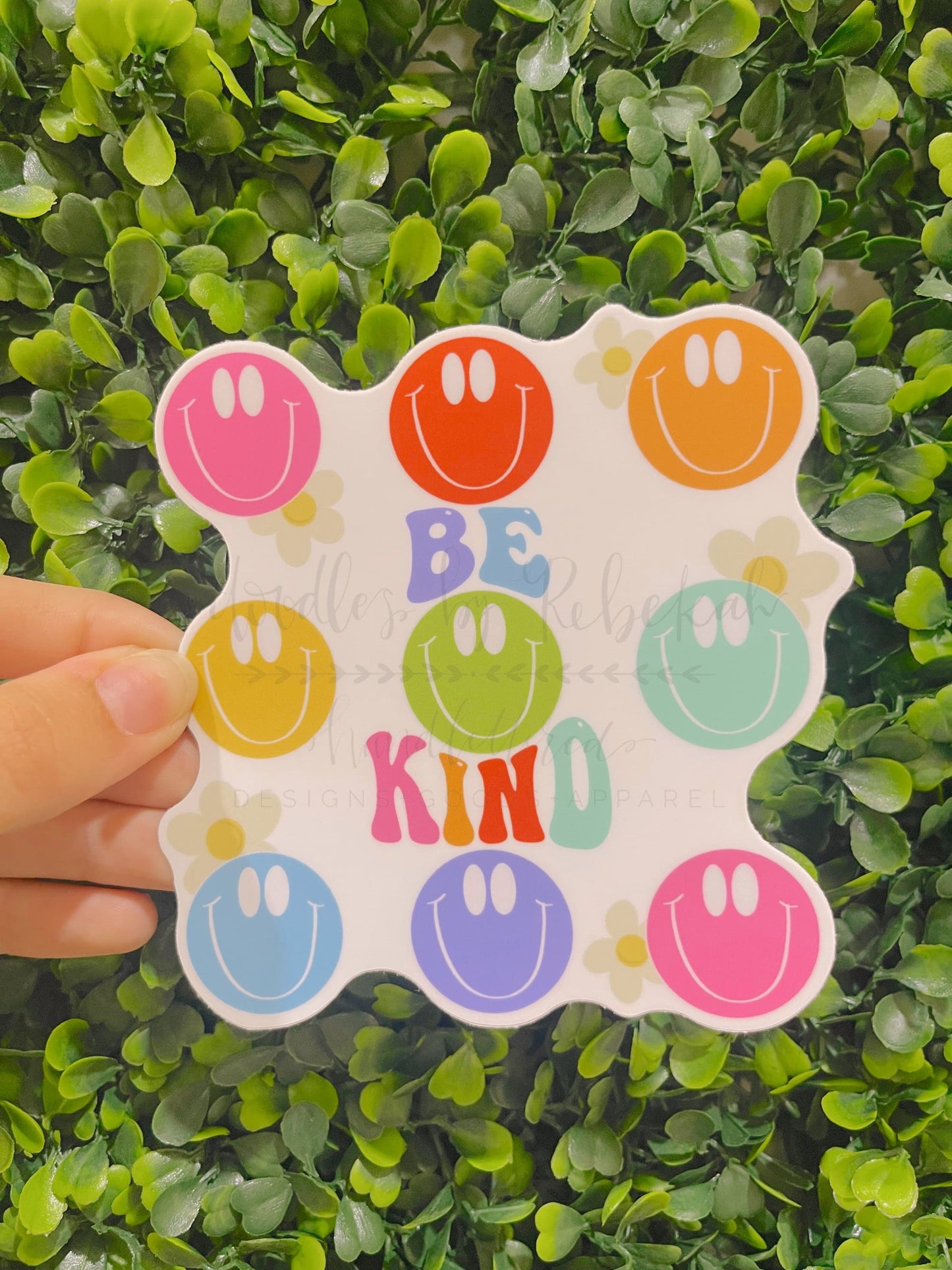 Person holding a vinyl sticker with multiple smiley faces and phrase "Be Kind"