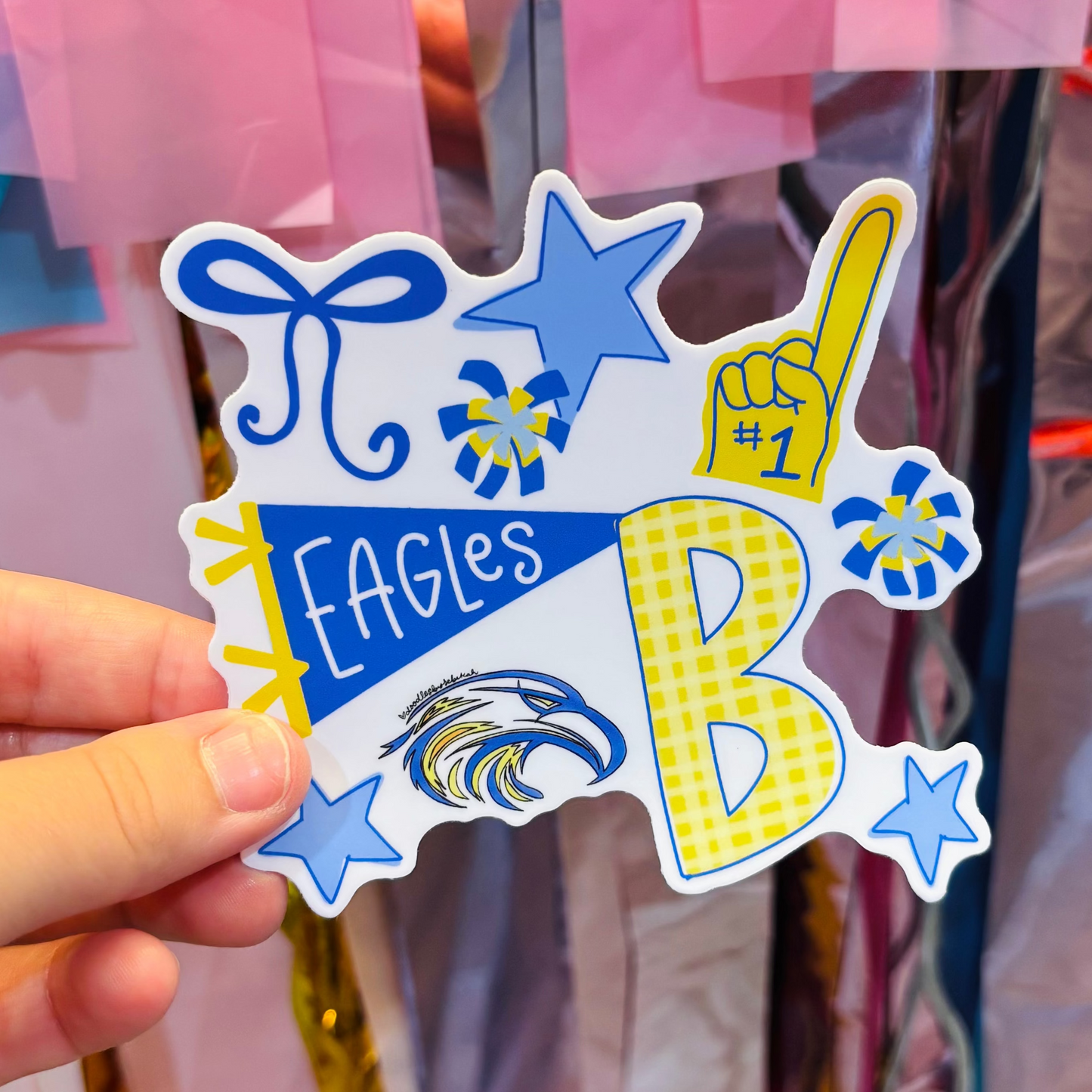 a hand holding a blue and yellow sticker with Team Eagles hand draw iconography