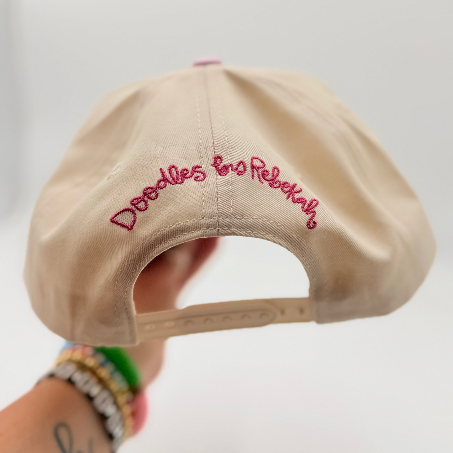 Beige cap with pink text held by a person against a white background