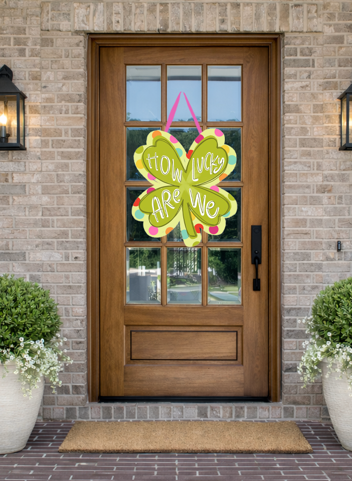Doodles by Rebekah St. Patrick's Day door decor featuring a whimsical "How Lucky Are We" shamrock illustration on a rustic front porch.