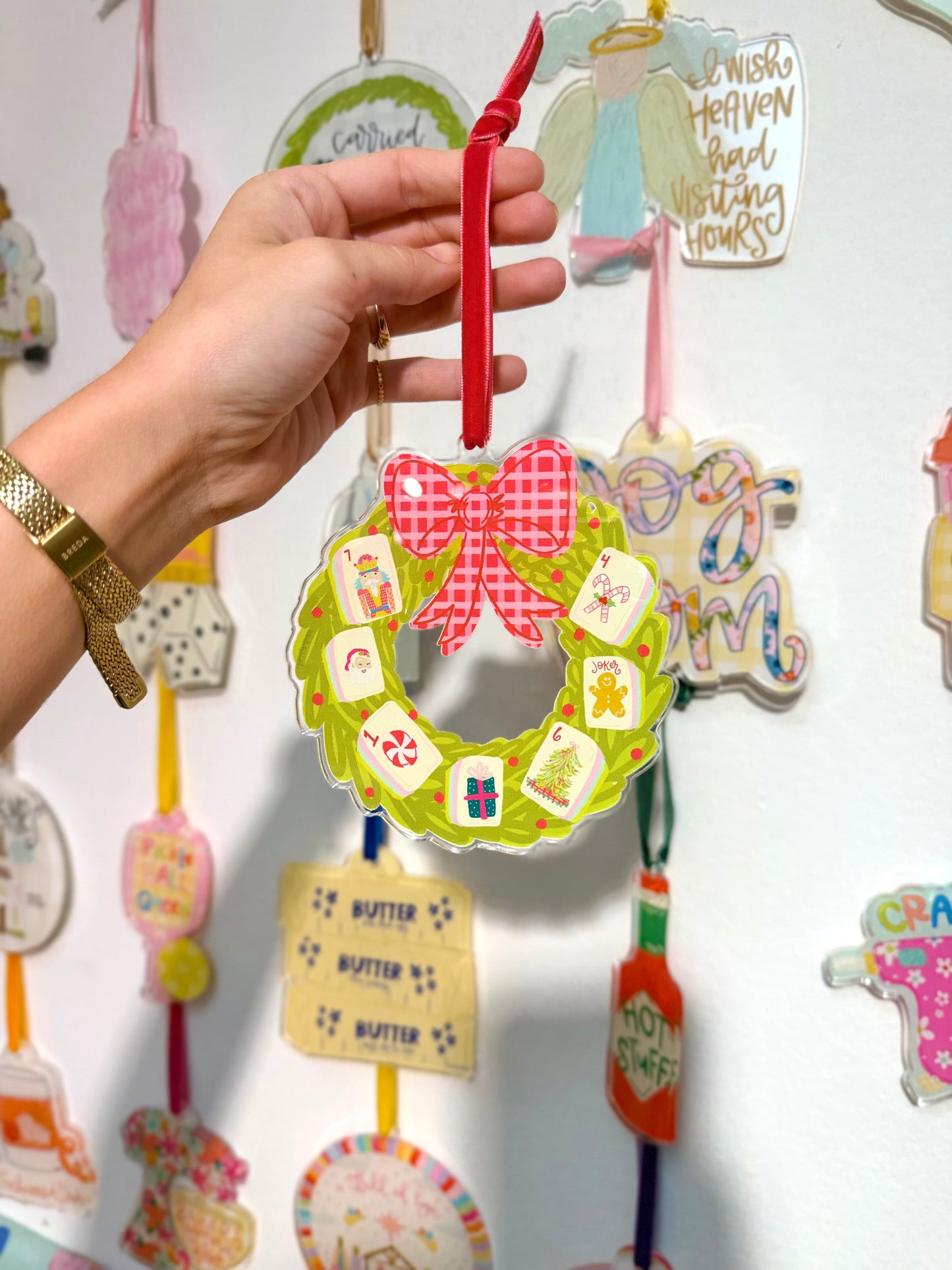 A Mahjong wreath acrylic ornament being held in front of an ornament wall