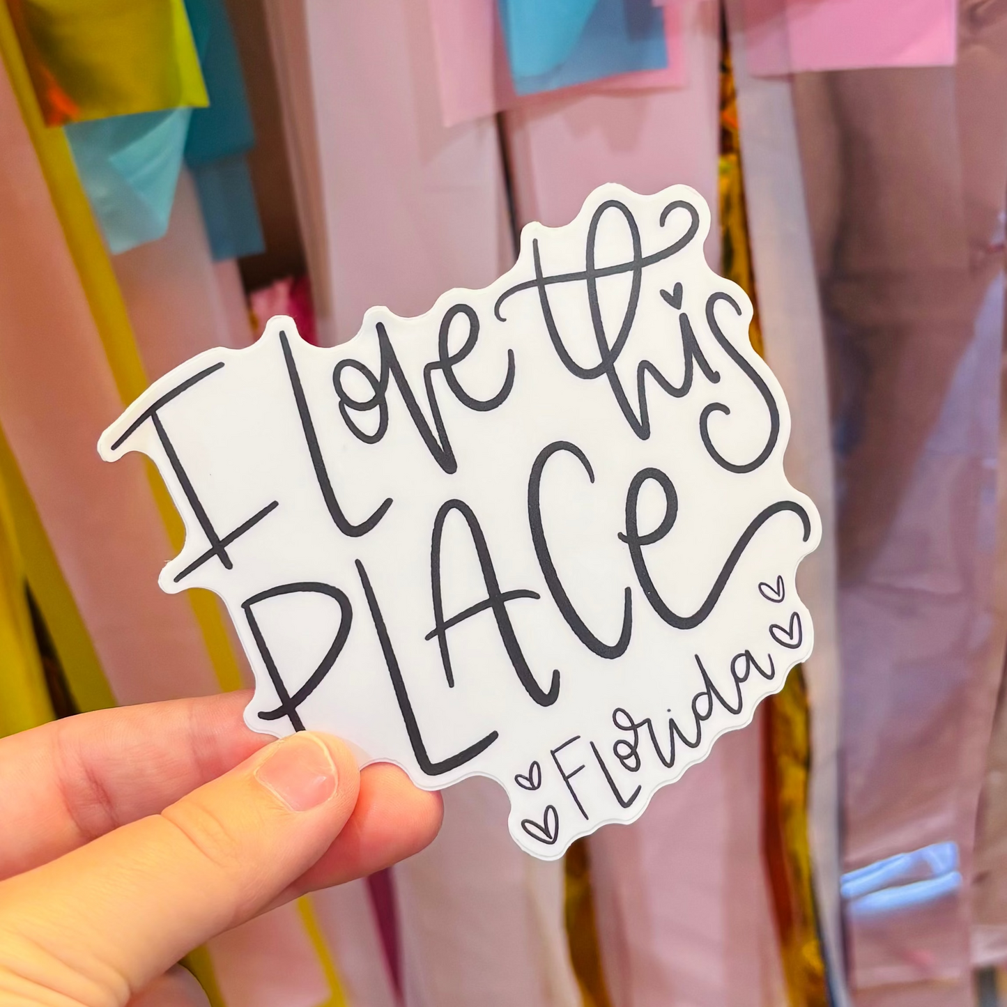 a hand holding a black and white sticker that reads "I Love This Place Florida"