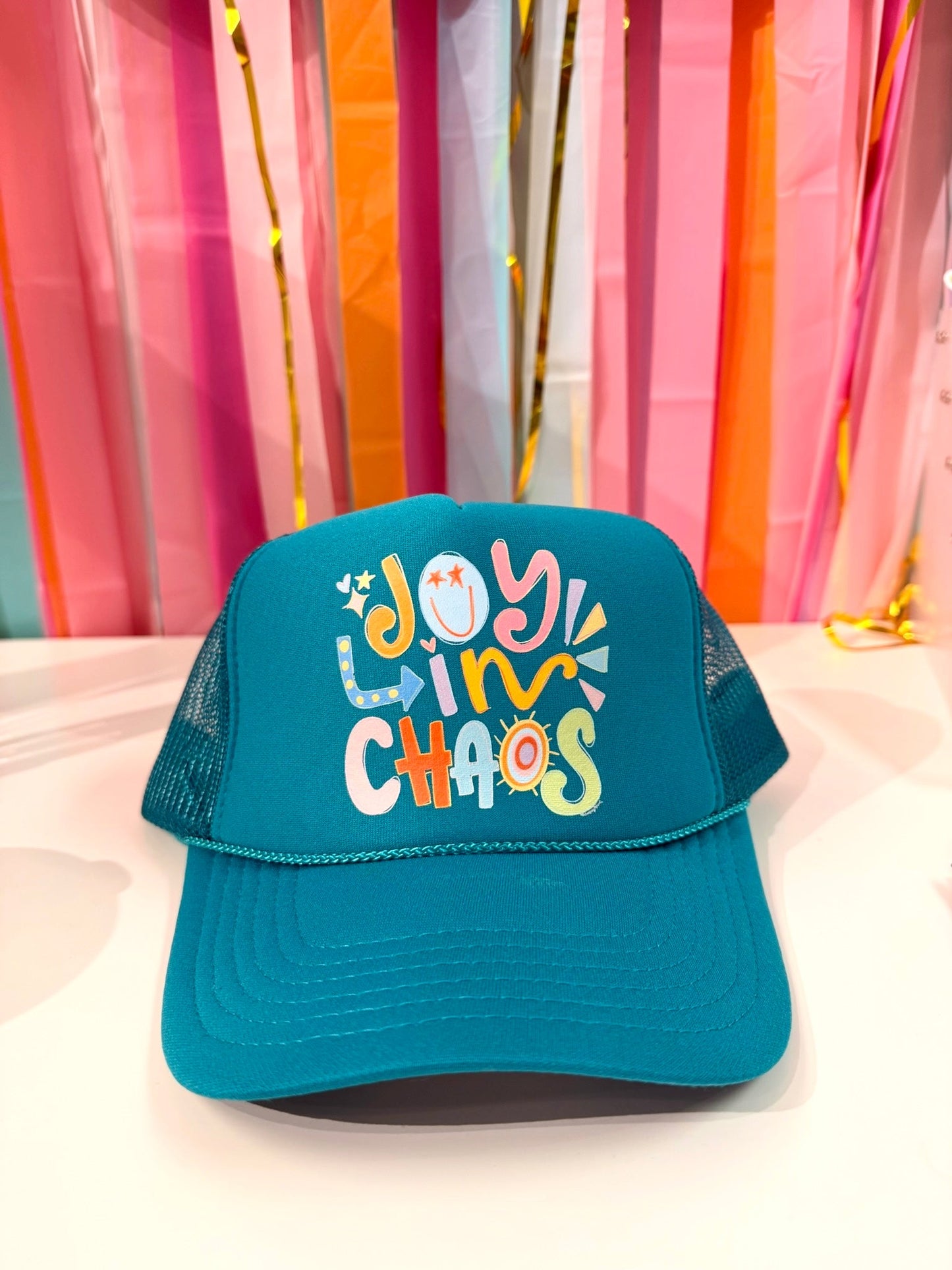 Doodles by Rebekah "Joy in Chaos" teal trucker hat featuring a whimsical hand-drawn typography design with colorful sun and star accents.