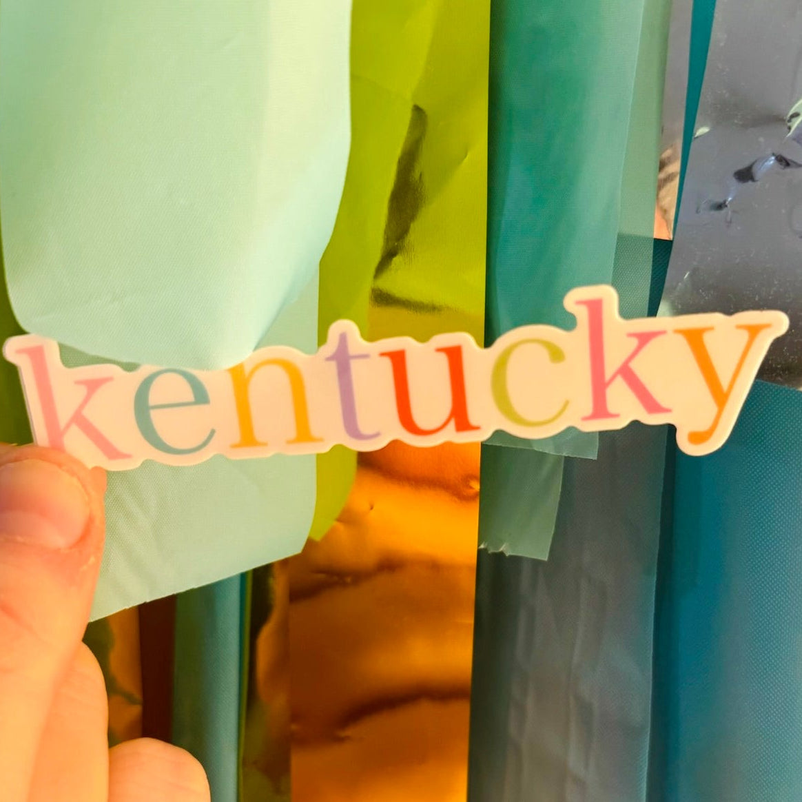 Doodles by Rebekah rainbow Kentucky typography sticker. This colorful hand-painted vinyl decal features a modern pastel palette, making it a perfect state pride gift for decorating water bottles, laptops, and planners for KY residents and travelers.