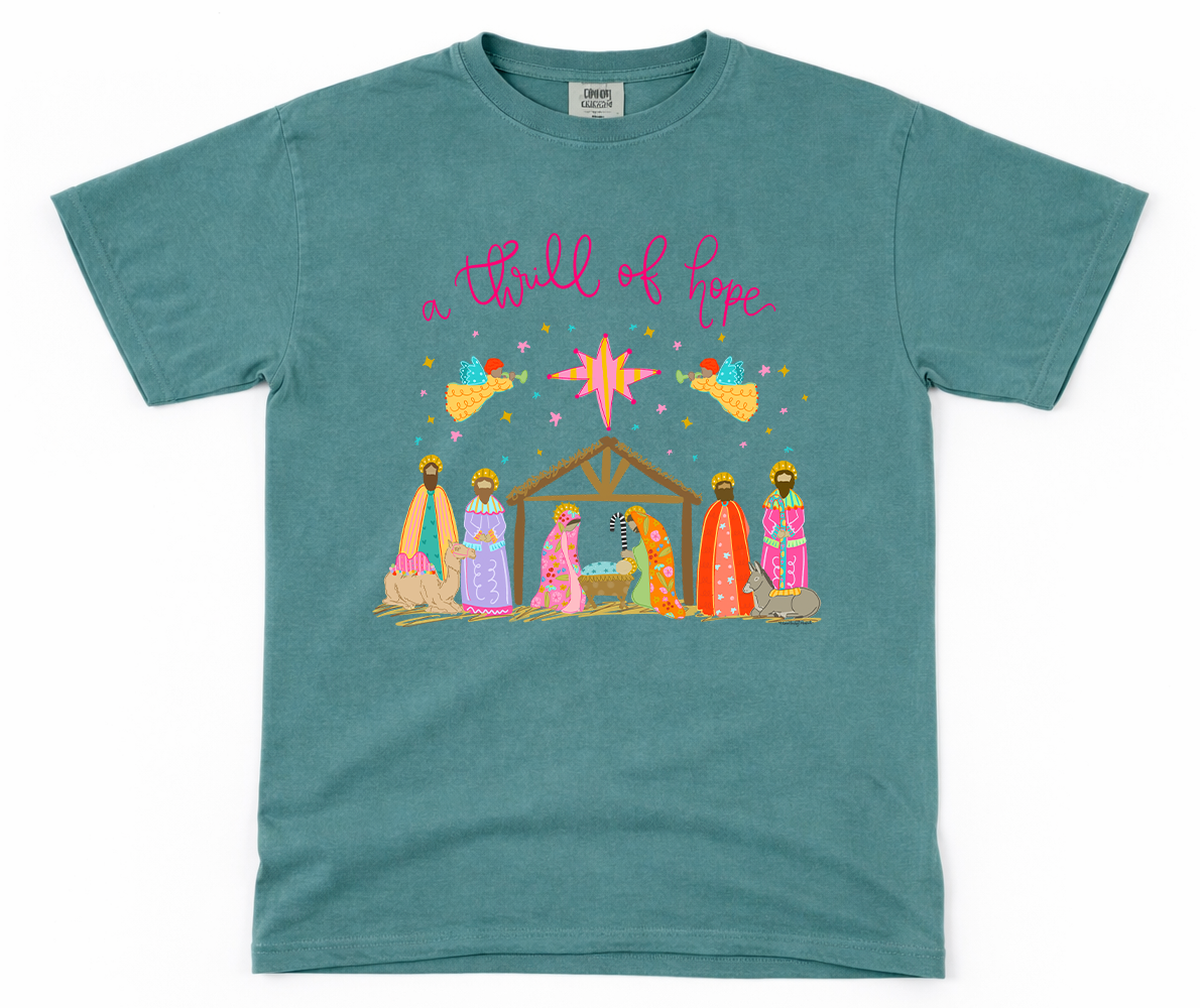 Teal t-shirt with nativity scene graphic and 'a thrill of hope' text on a white background