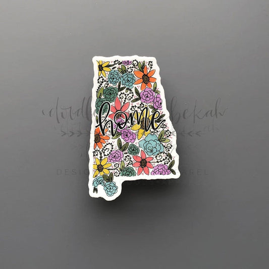 A sticker with an Alabama floral design on a white background with the word 'home' written on it. The sticker features various colored flowers and a purple outline of the state of Alabama.