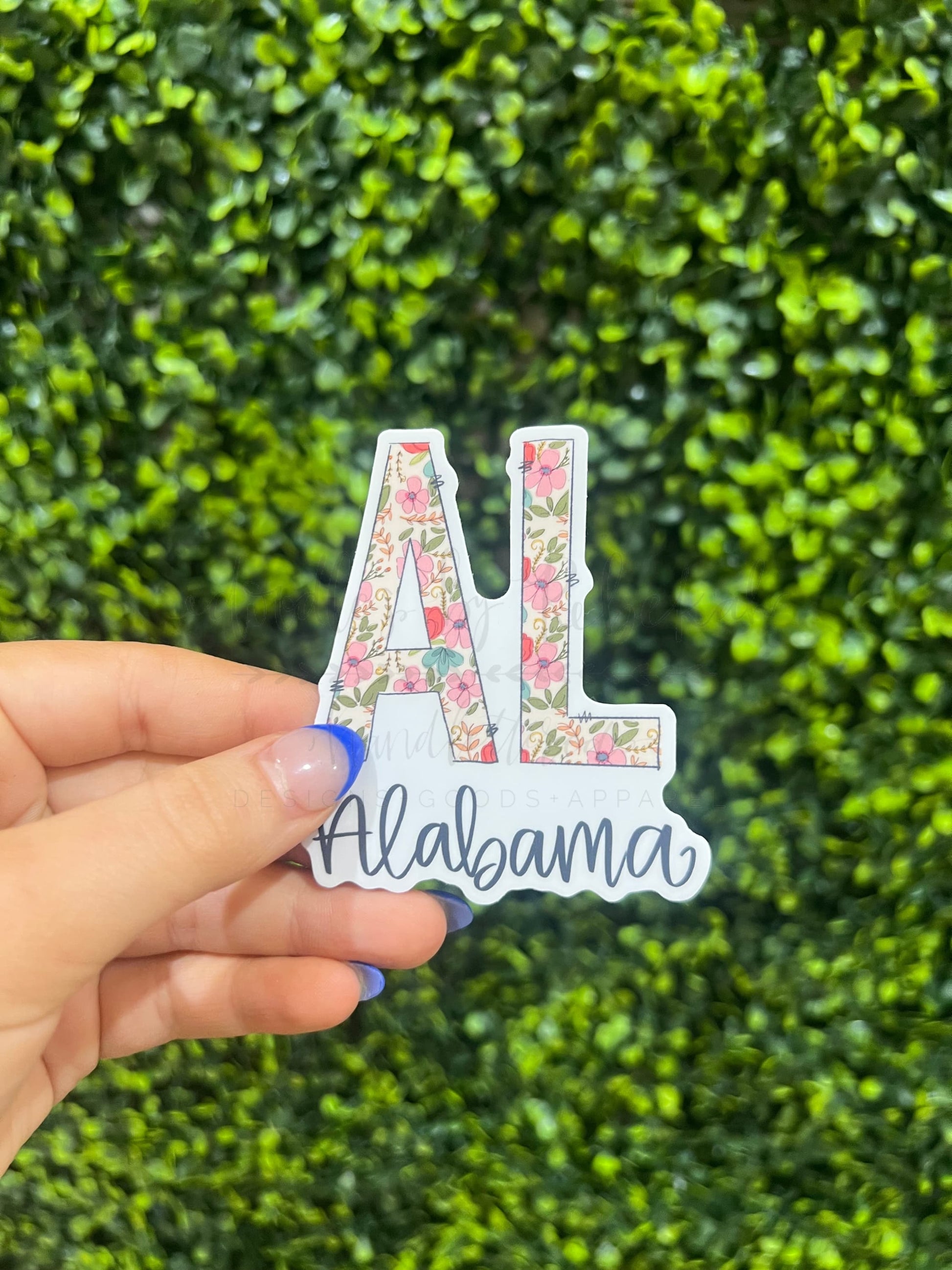 Someone holding a sticker with a floral AL and the word Alabama written at the bottom