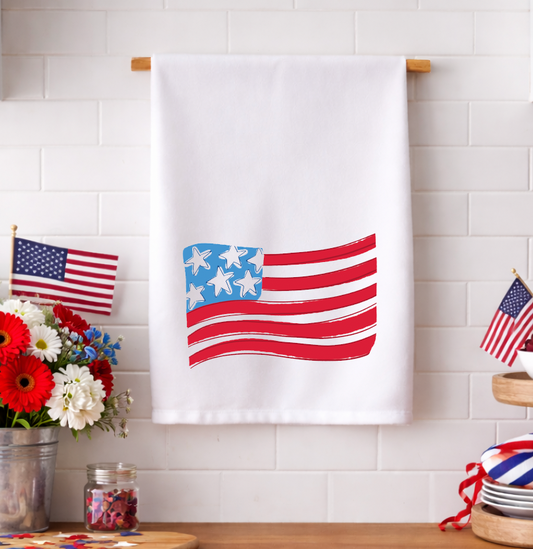Patriotic American flag tea towel with a whimsical hand-drawn design displayed in a bright kitchen with red, white, and blue decorations.