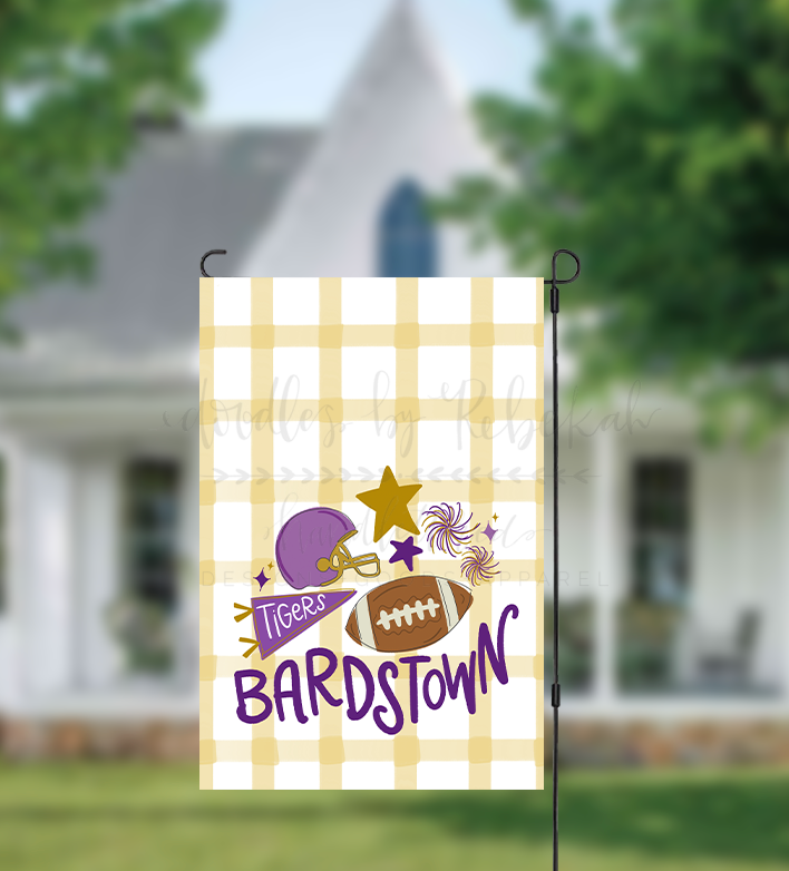 A rectangular plaid garden flag with a purple and yellow checkered pattern, featuring a logo of a helmet and a football, and the text 'BARDSTOWN'.