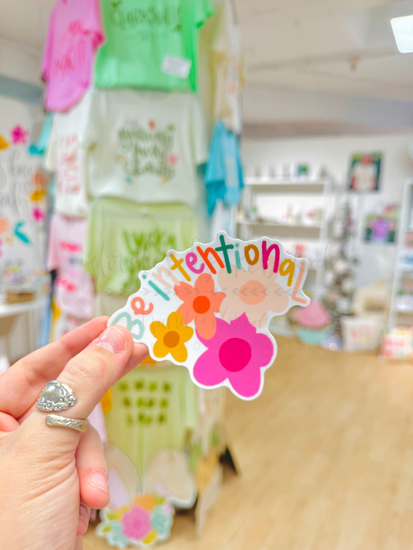 Person holding a vinyl sticker with flower graphic and phrase "Be intentional"