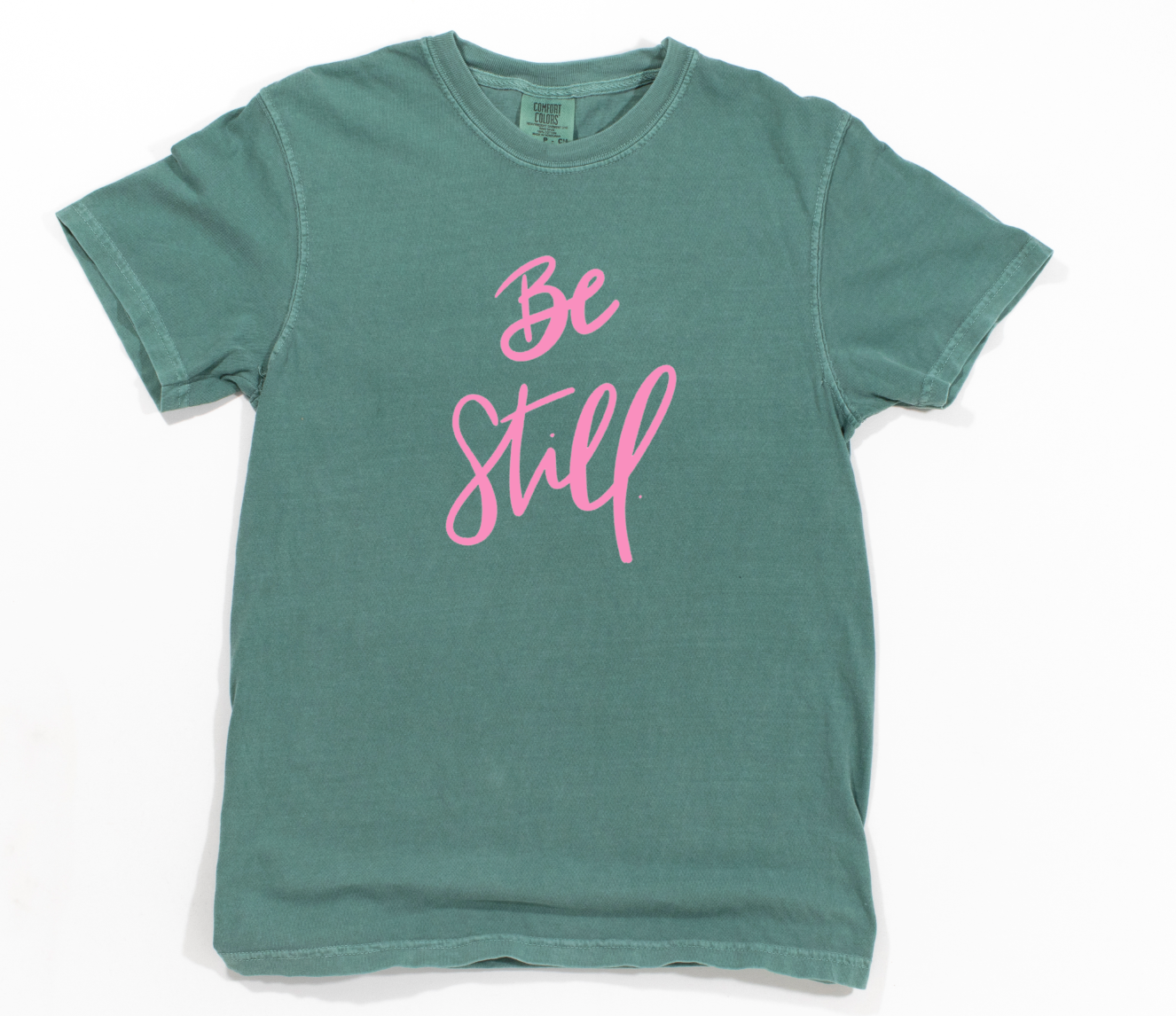 Green t-shirt with 'Be Still' in pink text on a white background