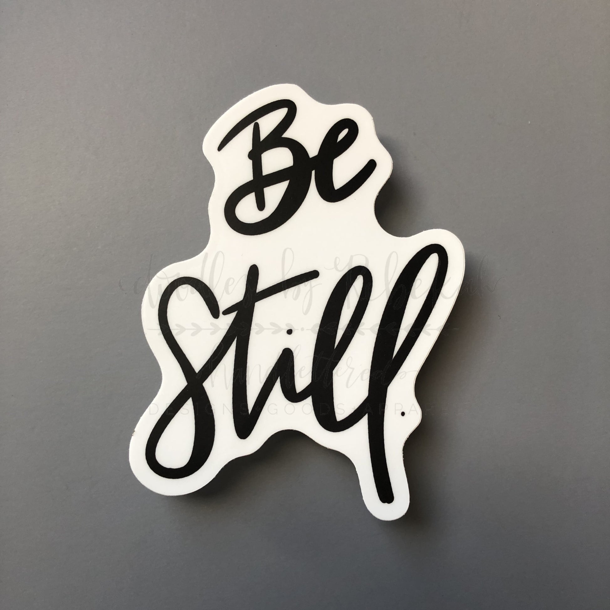 A white sticker with the phrase 'Be Still' written in a flowing black script font.