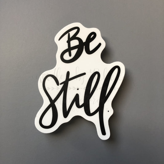 A white sticker with the phrase 'Be Still' written in a flowing black script font.