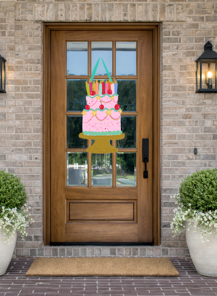 Doodles by Rebekah birthday door decor featuring a whimsical pink cake illustration with candles and cherries on a rustic front porch.