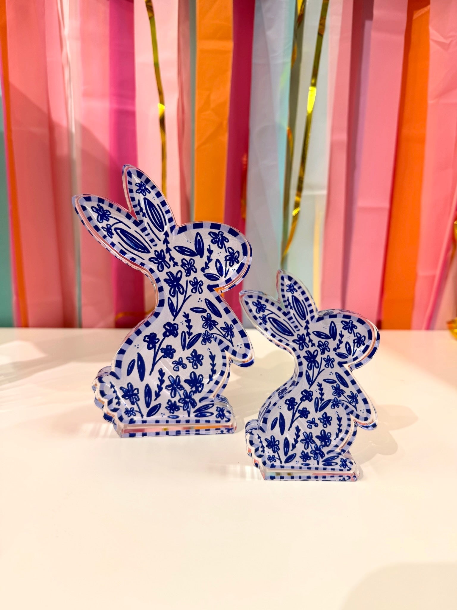 Doodles by Rebekah ginger jar bunny acrylic home decor featuring whimsical hand-painted navy and white chinoiserie floral patterns. These elegant spring bunny accents are shown against a bright party streamer background.