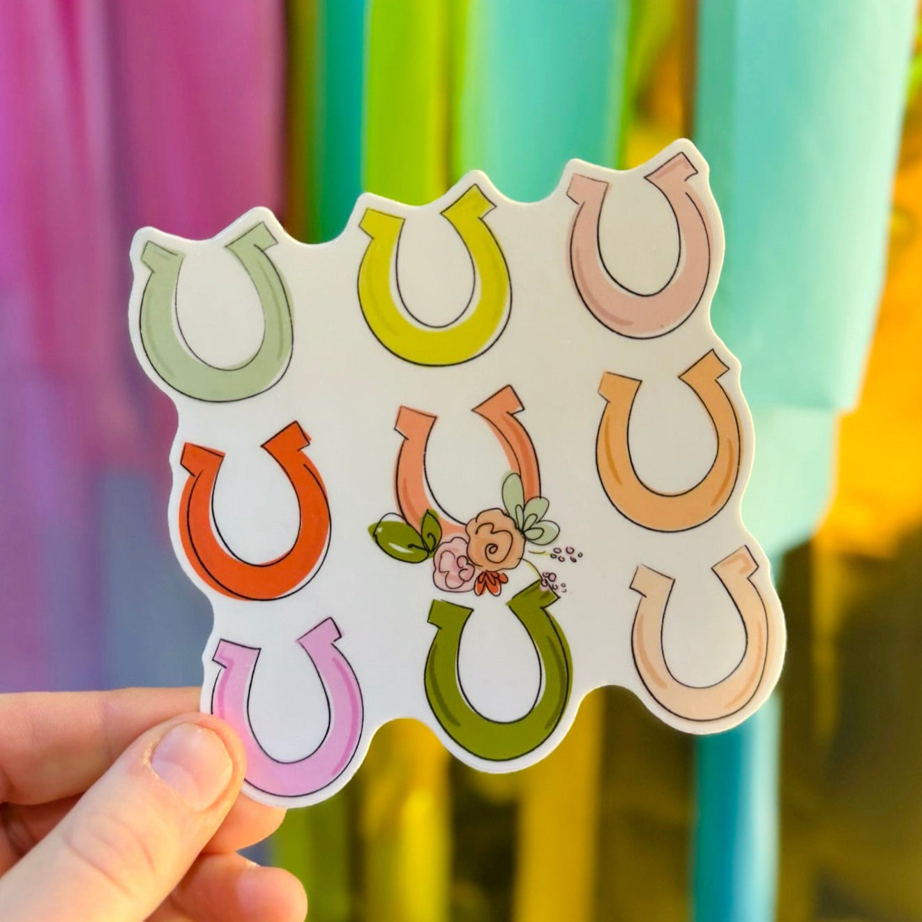 Doodles by Rebekah horseshoe and floral vinyl sticker. This whimsical hand-painted decal features colorful pastel horseshoes and a small rose bouquet, making it a perfect gift for horse lovers and equestrians to decorate water bottles, laptops, and planners.