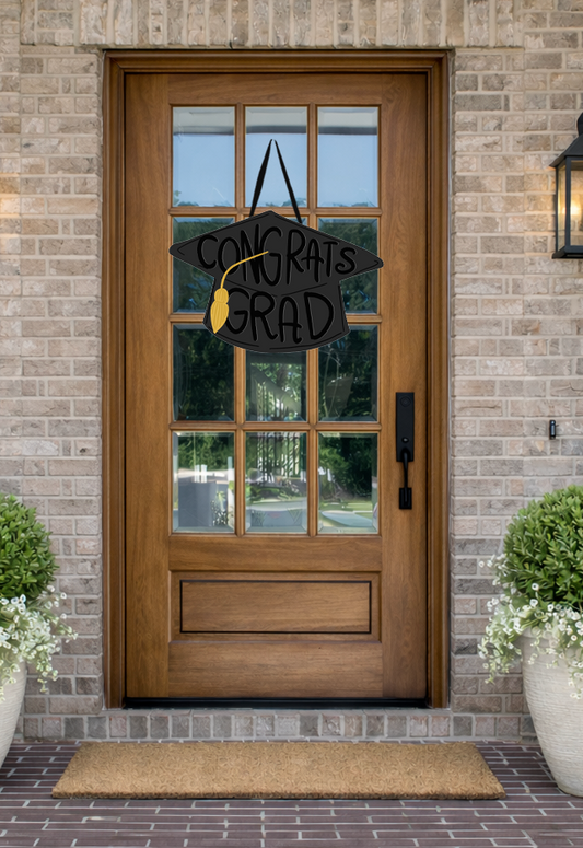 Doodles by Rebekah graduation door decor featuring a whimsical black grad cap illustration with a gold tassel on a rustic wooden front door.