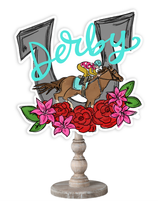 Doodles by Rebekah Kentucky Derby tabletop decor featuring a whimsical horse racing illustration, red roses, pink lilies, and teal "Derby" hand-lettering on a rustic wood stand.