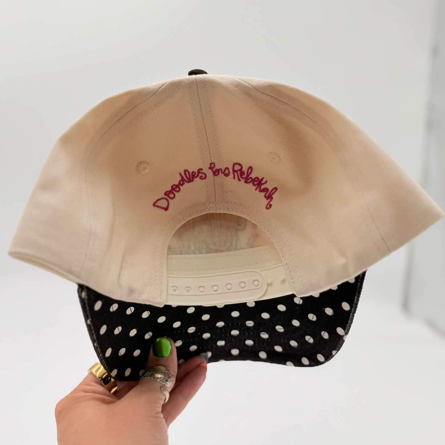 Beige cap with text held by a hand against a white background