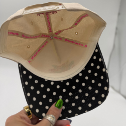 Black polka dot cap with beige interior held by a hand against a white background