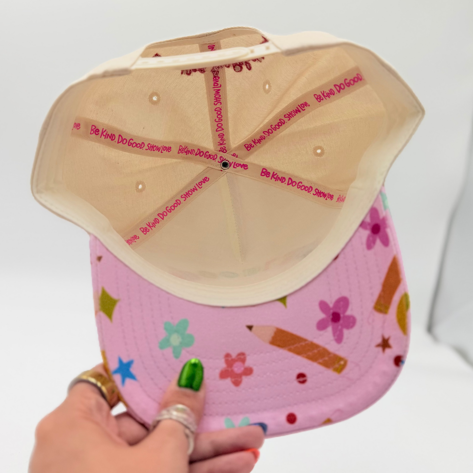 Hand holding a pink cap with colorful patterns against a white background