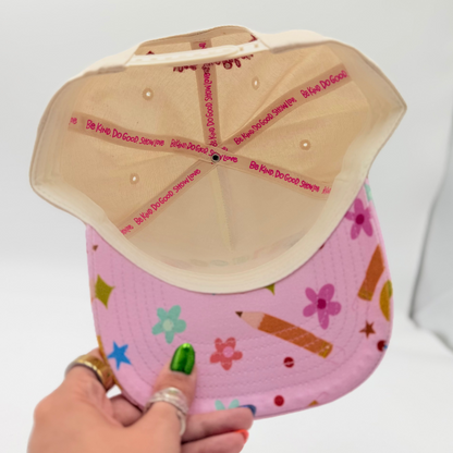 Hand holding a pink cap with colorful patterns against a white background