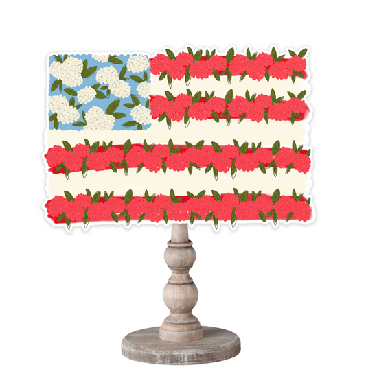 A stylized American flag topper made of white hydrangeas and red roses on a wooden dowel shown on a white background