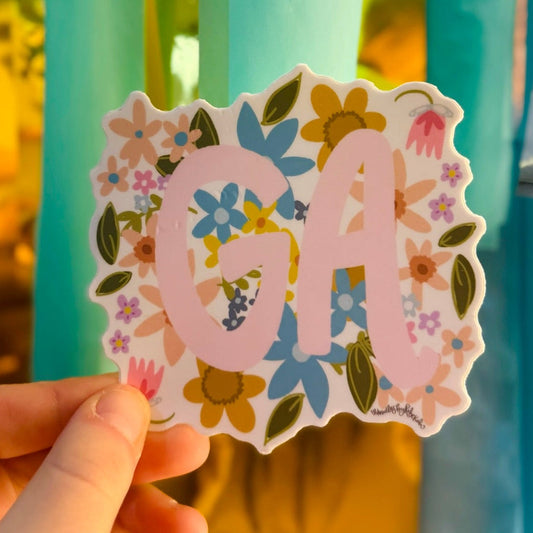 Doodles by Rebekah Georgia "GA" state pride floral sticker. This whimsical hand-painted vinyl decal with botanical accents and pink lettering is a perfect gift for Georgians to decorate water bottles, laptops, and planners.
