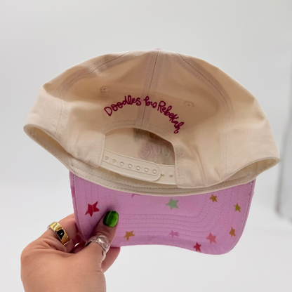 Hand holding a beige and pink cap with star patterns against a white background