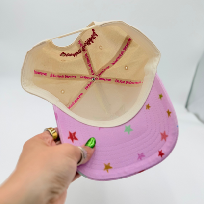 Hand holding a pink cap with star patterns against a white background