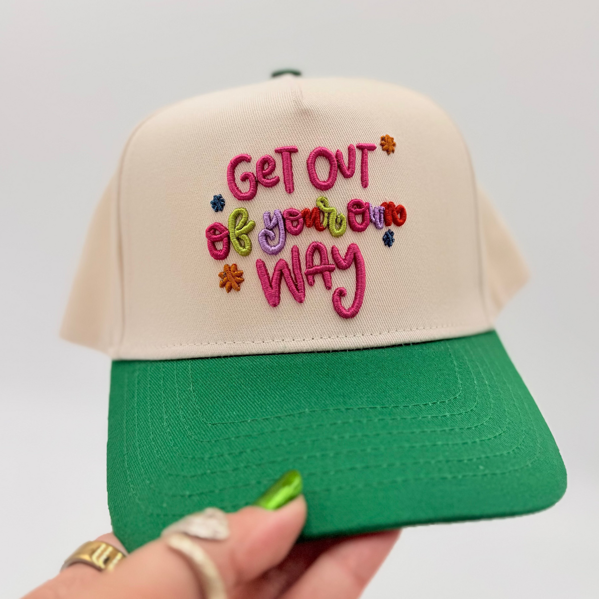Green and beige cap with colorful text held by a hand against a white background