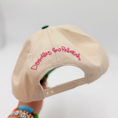 Beige cap with pink text held by a hand against a white background