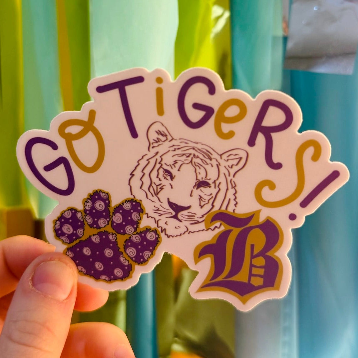 Doodles by Rebekah "Go Tigers!" school spirit sticker. This custom hand-painted vinyl decal in purple and gold features a tiger mascot and paw print, making it a perfect gift for students, teachers, and fans to show their team pride on water bottles or laptops.
