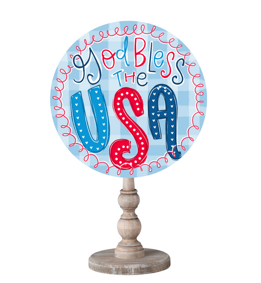 A circle topper with a blue and white plaid background that reads "God Bless the USA" on a wooden dowel holder