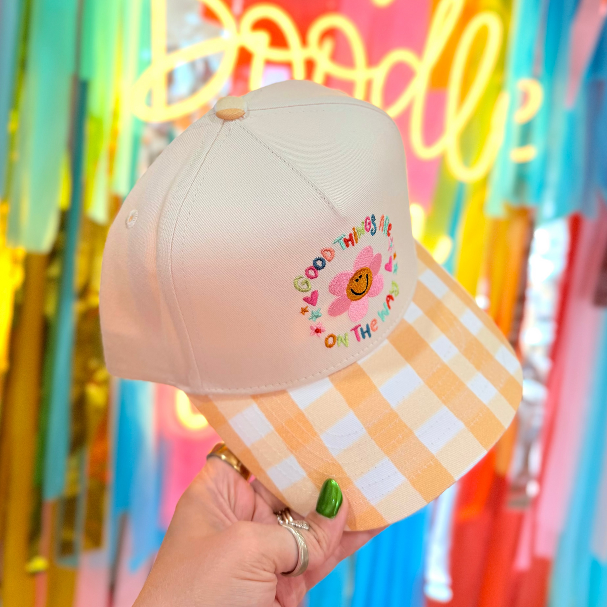 Pink cap with colorful text and checkered pattern held in front of a vibrant, multicolored background with 'One Doodle' neon sign.