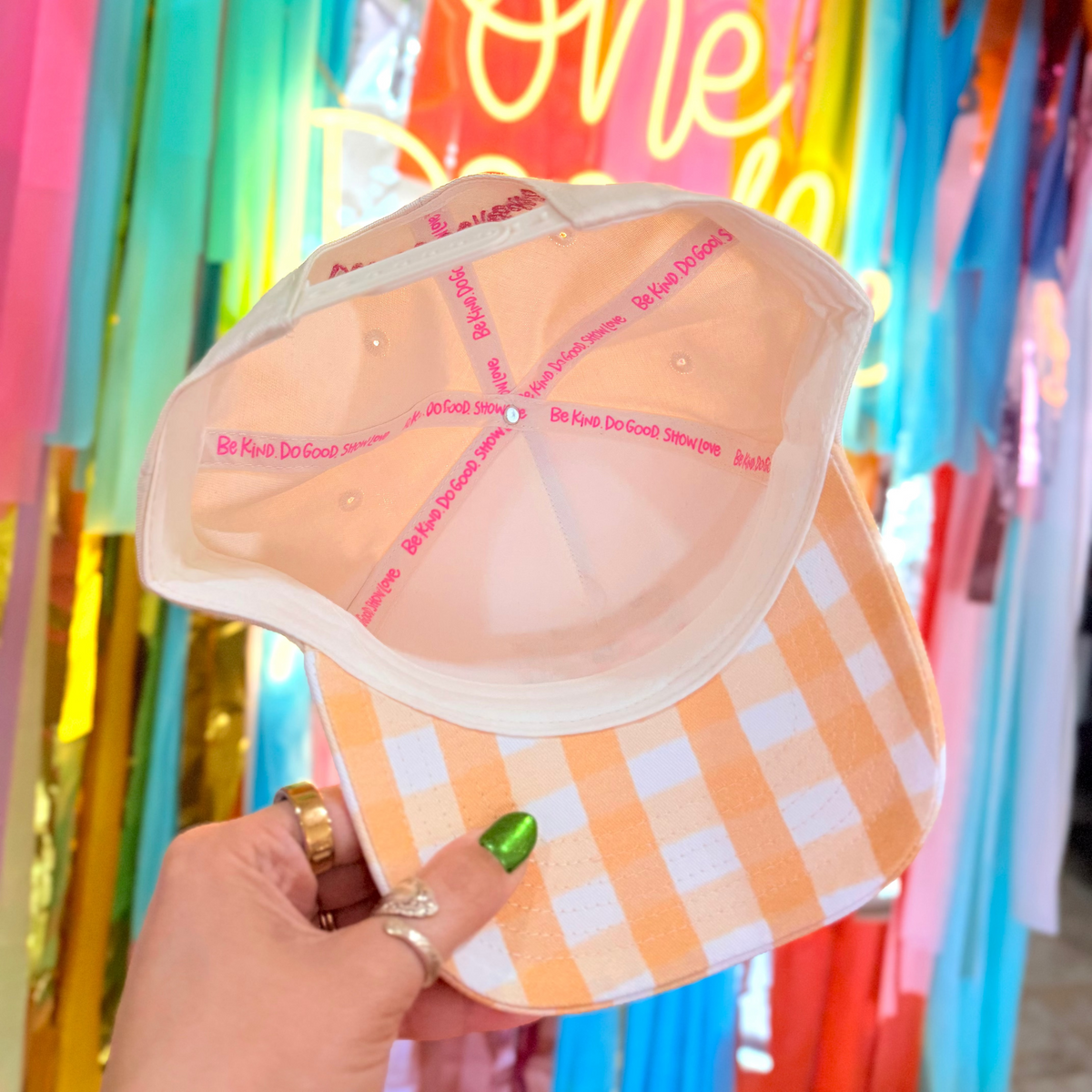 Checkered bikini hat held in front of a colorful 'One Dozen' neon sign and streamers.