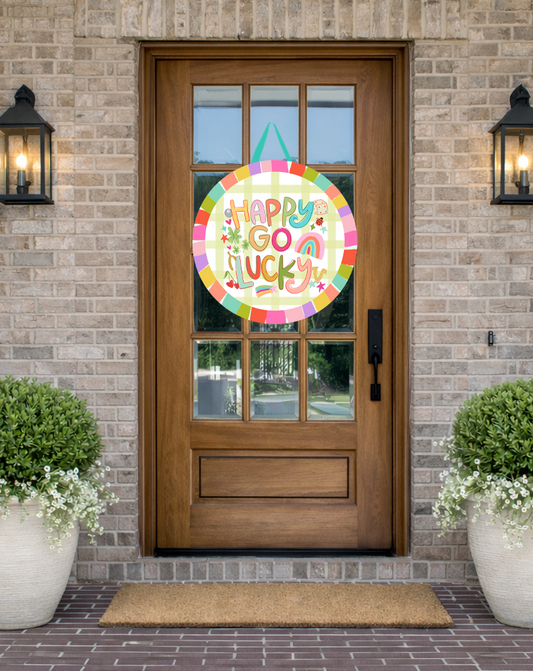 Doodles by Rebekah St. Patrick's Day door decor featuring a whimsical "Happy Go Lucky" illustration with rainbow and shamrock motifs on a rustic front porch.