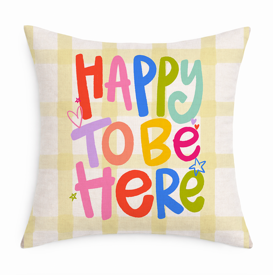 A colorful pillow that reads "Happy To Be Here" on a white background