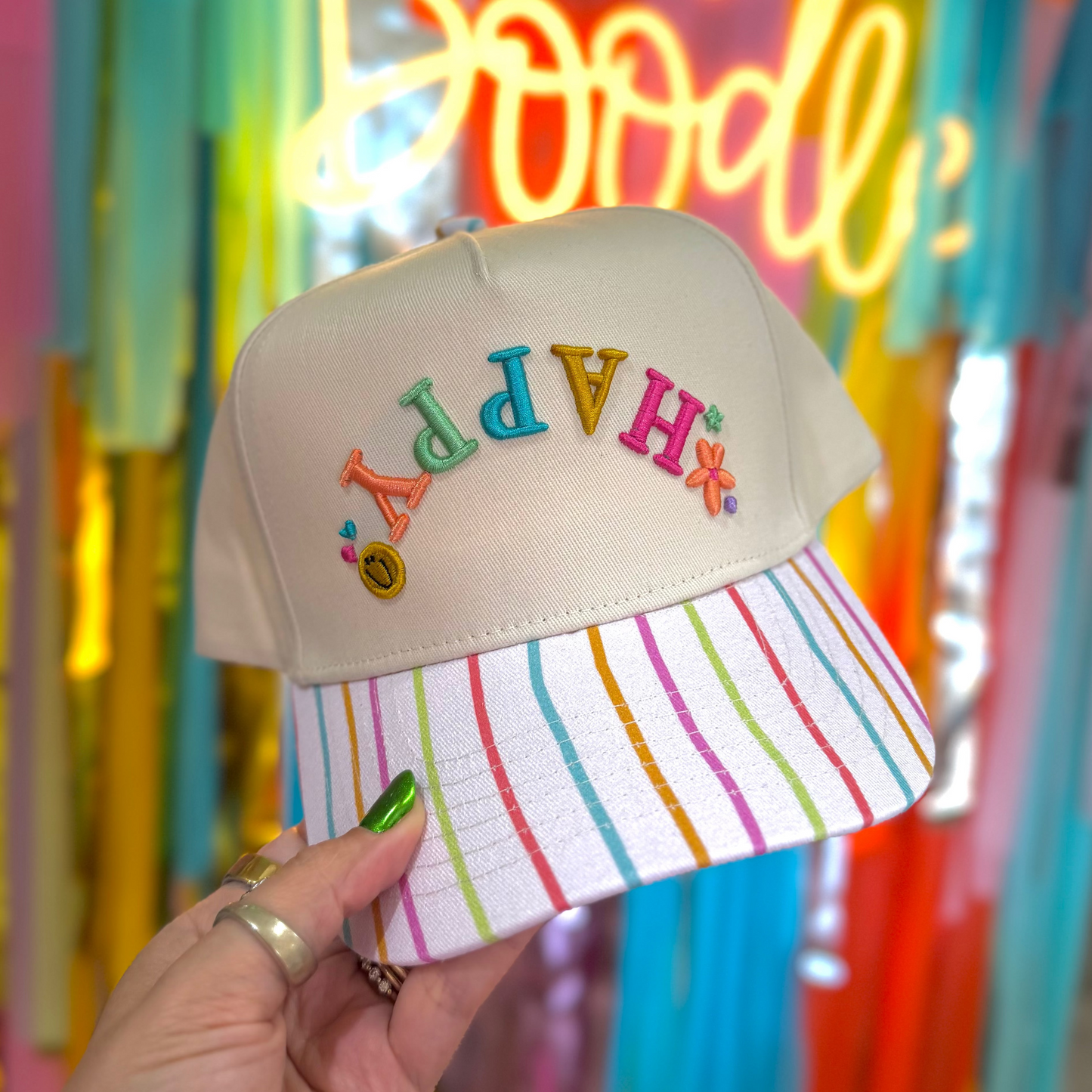 Colorful cap with embroidered letters held in front of a neon sign.