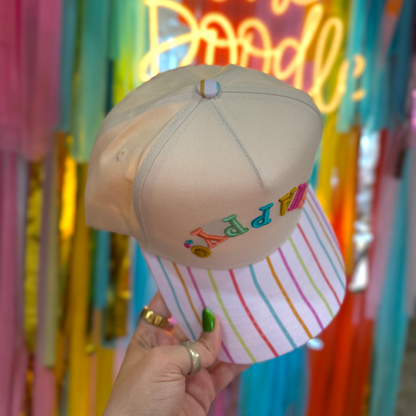Beige cap with colorful text held in front of a vibrant, multicolored background with neon lights.