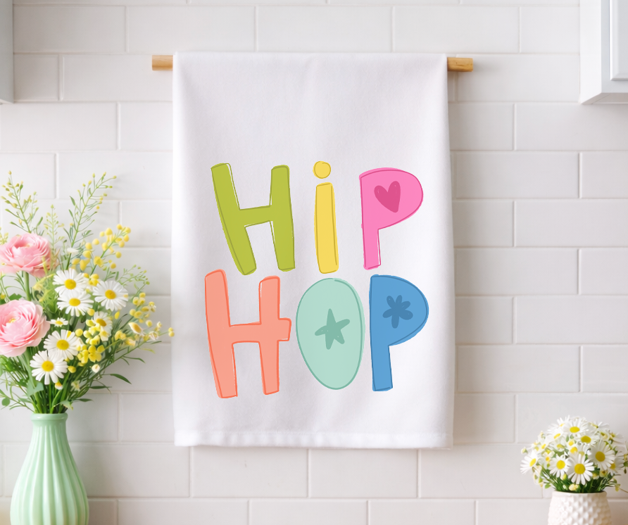 Whimsical "Hip Hop" Easter decorative tea towel with colorful hand-lettered typography, displayed in a bright kitchen with fresh spring floral arrangements.