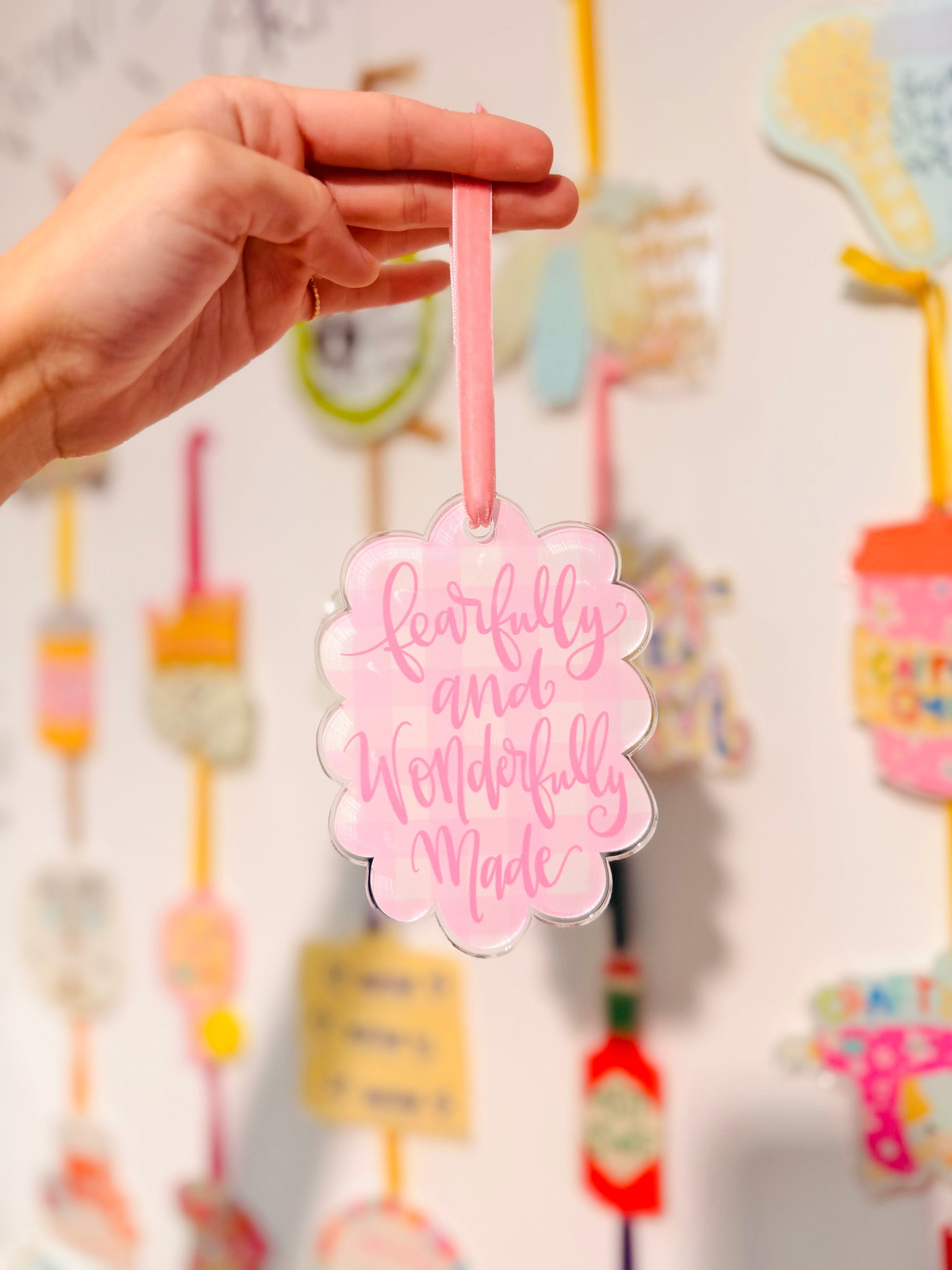 Hand holding a pink ornament with 'Fearfully and Wonderfully Made' text against a colorful background.
