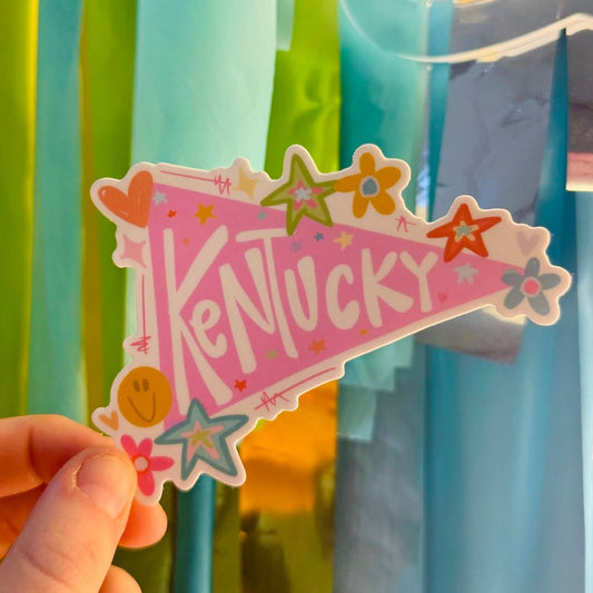 Doodles by Rebekah Kentucky pennant vinyl sticker. This whimsical pink state pride decal features hand-painted retro icons and stars, making it a perfect gift for KY residents and college students to decorate water bottles, laptops, and dorm rooms.