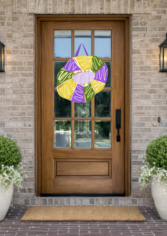 Doodles by Rebekah Mardi Gras door decor featuring a hand-drawn King Cake illustration in traditional purple, green, and gold colors on a rustic front porch.