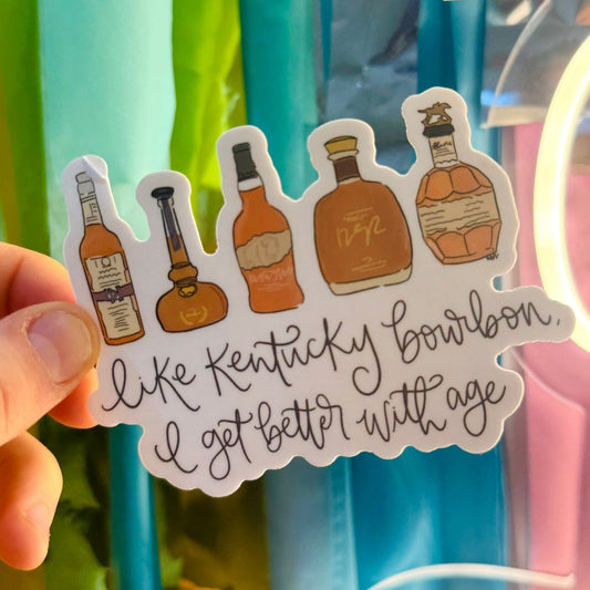Doodles by Rebekah "Kentucky Bourbon" birthday sticker. This whimsical vinyl decal features five different bourbon bottles and an inspirational aging quote, making it a perfect birthday gift for bourbon lovers to display on water bottles, laptops, and home bars.