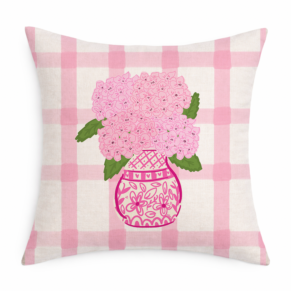 A gingham pillow with pink hydrangeas in a pink vase on a white background