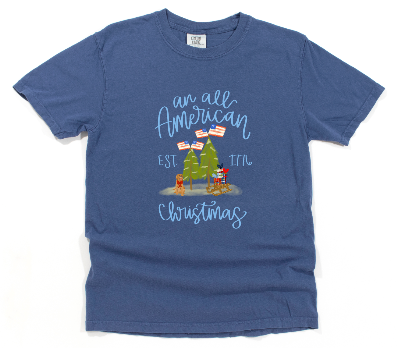 Blue t-shirt with Christmas-themed design featuring trees and flags with 'an all American Christmas, EST. 1776' text on a white background