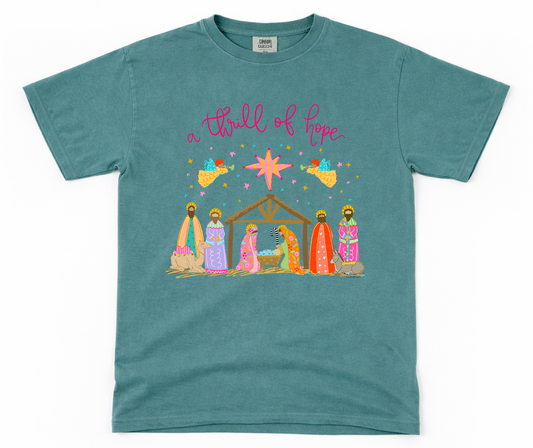 Teal t-shirt with nativity scene graphic and 'a thrill of hope' text on a white background