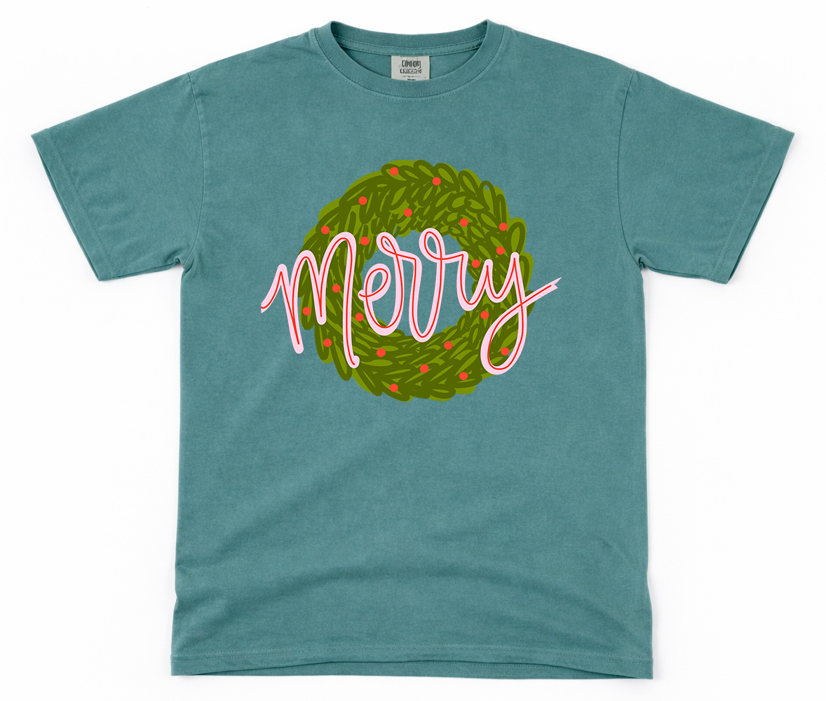 Teal t-shirt with 'Merry' wreath design on a white background